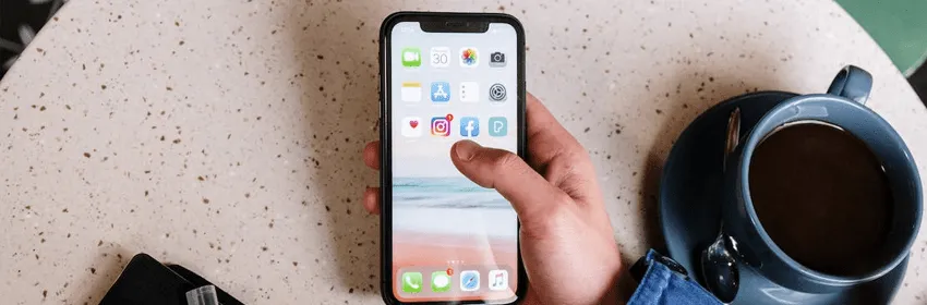 Ruka držící telefon s aplikací sociální sítě u šálku kávy